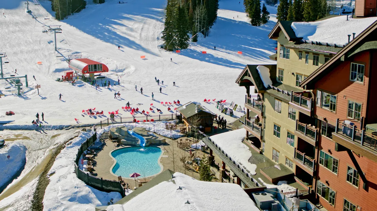 This lively exterior scene shows the lodge buildings beside ski slopes, a sparkling swimming pool, and a ski lift—capturing guests enjoying both winter sports and poolside relaxation. The image brings together the thrill of skiing with the luxury of resort amenities all in one frame.
