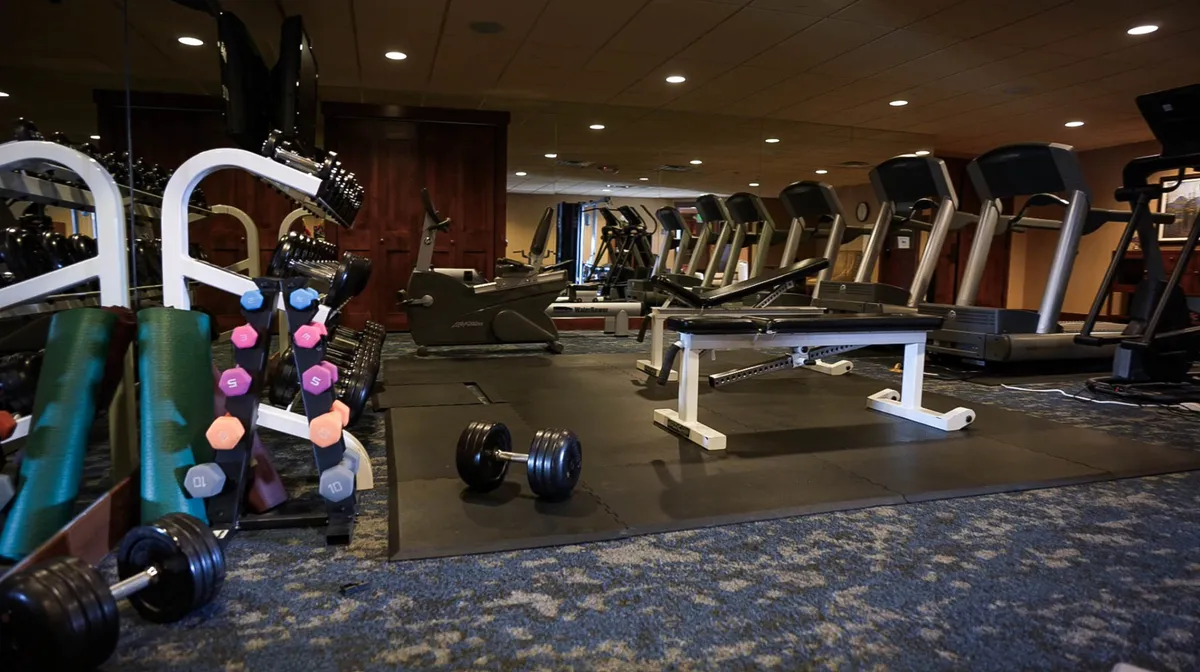 A motivational, well-equipped fitness center featuring dumbbells, treadmills, and a weight bench, encouraging personal fitness and group activity. The space is bright and inviting, ideal for a midday break.