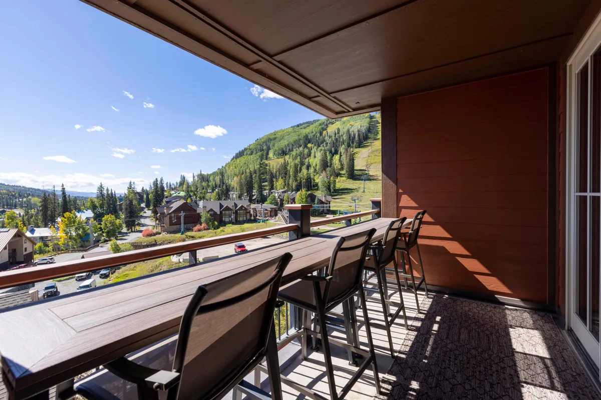 A cozy outdoor bar seating area with a stunning mountain view and lush greenery, perfect for morning coffee, outdoor dining, or evening gatherings. The image exudes relaxation and togetherness amidst a beautiful alpine backdrop.