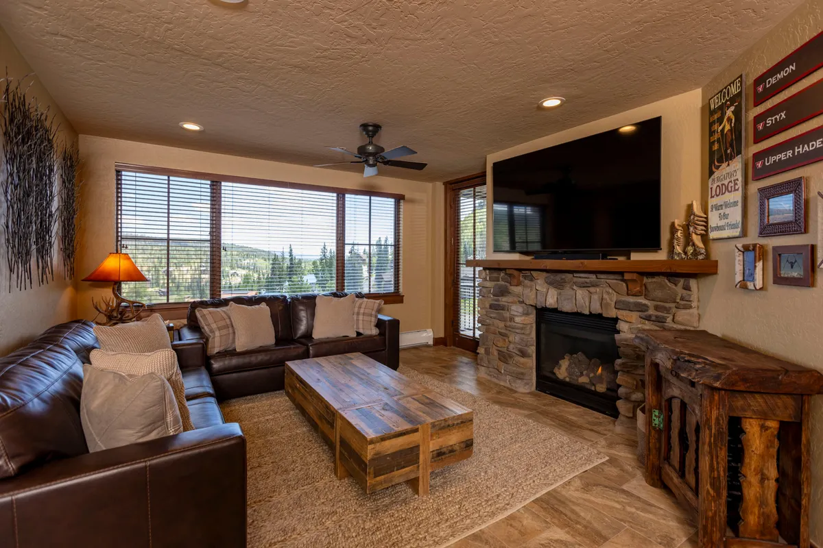 This image showcases a welcoming living room centered around a plush leather sofa, a coffee table perfectly placed for group activities, a fireplace that adds warmth and ambiance, large windows that invite in natural light, and a prominent television ideal for movie nights or big games.