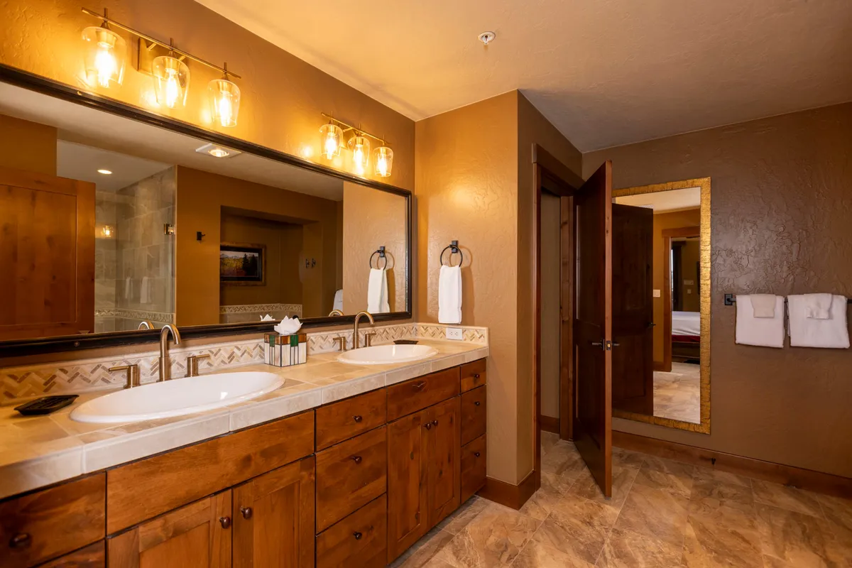 A modern bathroom with a double sink vanity, expansive mirror, and elegant light fixtures. The clean lines and upscale finishes evoke a spa-like ambiance, ideal for relaxing after a day of adventure.