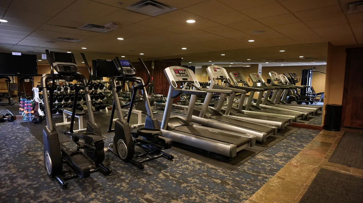 A modern, fully equipped fitness center featuring treadmills, elliptical machines, and a dumbbell rack. Expansive mirrors and bright lighting create an inviting atmosphere for health and wellness routines.