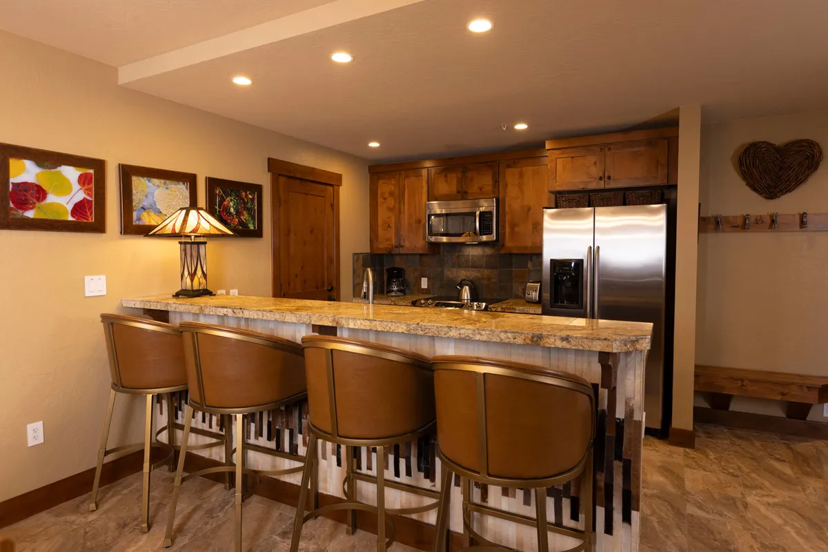 This image features a modern kitchen with a granite countertop, bar stools, stylish cabinetry, and prominent kitchen appliances. Decorative artwork and thoughtful design touches create an inviting atmosphere, while the spacious bar area encourages socializing and meal preparation.